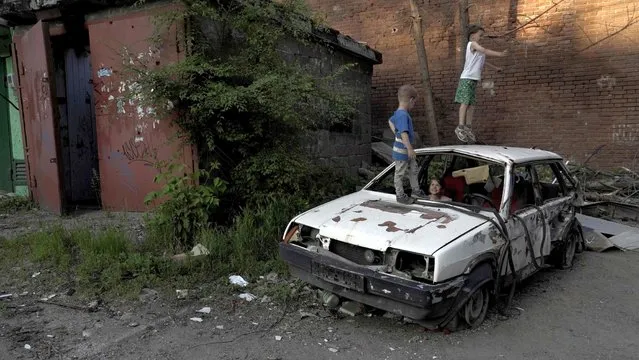 Children play on a destroyed car in a residential area of Mariupol on May 29, 2022, amid the ongoing Russian military action in Ukraine. (Photo by AFP Photo/Stringer)