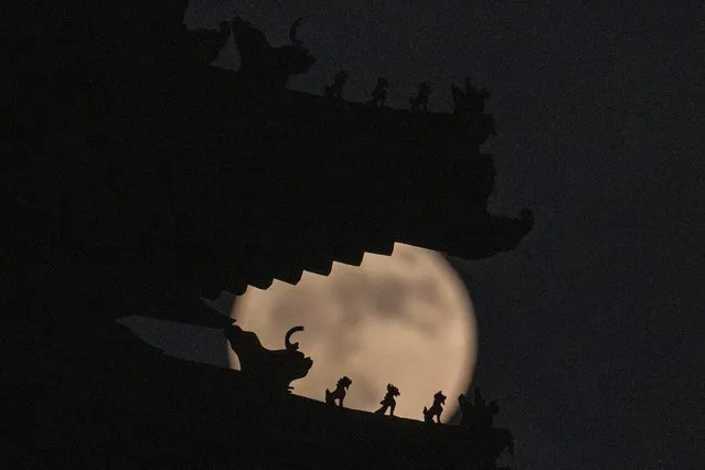 Roof decorations on the corner tower at the Forbidden City depicting sacred beasts are silhouetted against a supermoon, Tuesday, June 14, 2022, in Beijing. The moon reach its full stage on Tuesday, during a phenomenon known as a supermoon because of its proximity to Earth, and it is also labeled as the “Strawberry Moon” because it is the full moon at strawberry harvest time. (Photo by Ng Han Guan/AP Photo)
