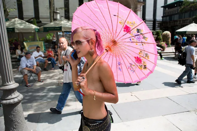 A topless woman walks through Bryant Park following the protest march called the GoTopless Day Parade Sunday, August 23, 2015, in New York. The parade took to the streets to counter critics who are complaining about topless tip-seekers in Times Square. Appearing bare-breasted is legal in New York. But Mayor Bill de Blasio and police Commissioner Bill Bratton say the body-painted women in the square who take photos with tourists are a nuisance. (Photo by Kevin Hagen/AP Photo)