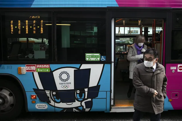 Passengers wearing masks get off a bus with the livery of Miraitowa, the official mascot of the Tokyo 2020 Olympics, in Tokyo, Thursday, March 5, 2020. Despite worldwide concern and speculation about whether the fast-spreading virus outbreak will affect the Tokyo Olympics, the IOC's leadership is not joining in the debate. (Photo by Jae C. Hong/AP Photo)