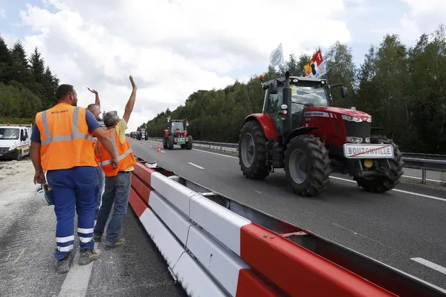 Workers wave to French farmers from Lorraine region as they drive their tractors on the A4 motorway in the Champagne-Ardenne region, eastern France, September 2, 2015. Hundreds of tractors were heading towards Paris for a protest due to take place on Thursday where French farmers will call for more help with low prices and high costs in the European Union's largest agricultural producer country. (Photo by Jacky Naegelen/Reuters)