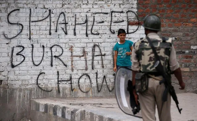 A boy stands next to a wall painted with graffiti as an Indian policeman stands guard during a protest in Srinagar against the recent killings in Kashmir, July 22, 2016. (Photo by Danish Ismail/Reuters)