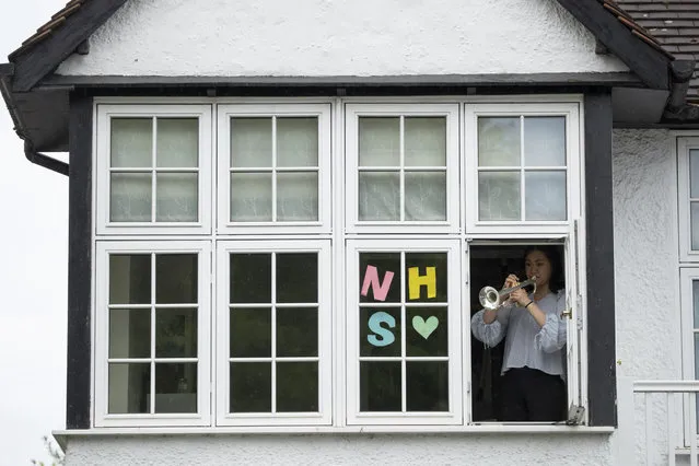 National Youth Orchestra of Great Britain trumpet player Tian Hsu, 16, takes part in a socially distanced orchestra performance of Beethoven's “Ode to Joy” from a window of her home in south west London, during the lockdown to try and stop the spread of coronavirus, Friday, April 17, 2020. The members of the National Youth Orchestra, took part in the coordinated Ode to Joy-a-thon on Friday, each giving their own 40 second performance, with photos or videos taken by their families to share on social media. They dedicated the performance to the National Health Service staff, key workers, and people who feel isolated in their homes during the lockdown. (Photo by Matt Dunham/AP Photo)