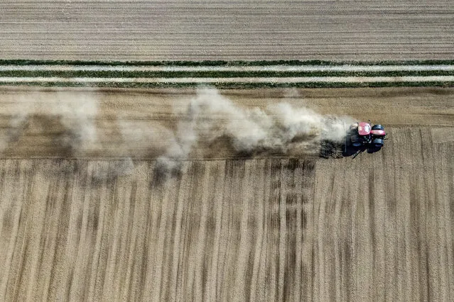 A farmer kicks up dust with his tractor while working on a field in Kleinpinning, Germany, Thursday, April 9, 2020. (Photo by Armin Weigel/dpa via AP Photo)