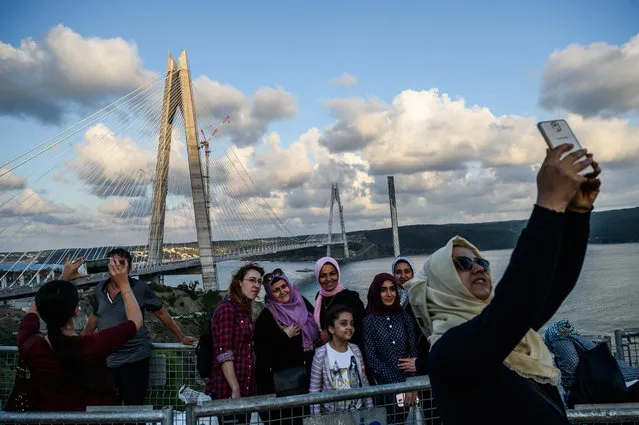 People take pictures with their cellphones as they pose next to the Yavuz Sultan Selim bridge on August 26, 2016 in Istanbul during the inauguration of the Yavuz Sultan Selim bridge. The bridge – technically a hybrid between a suspension and cable-stayed bridge – is an architectural marvel spanning the steep banks of the Bosphorus at the entrance to the Black Sea. It is the widest suspension bridge in the world with a width of 58.5 metres (192 feet). Its span of 1,408 metres (4,619 feet) is the longest in the world between the supporting pylons. (Photo by Ozan Kose/AFP Photo)