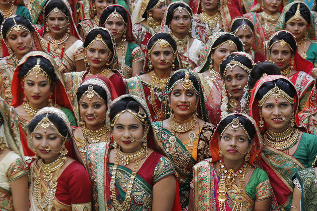 Indian brides pose for photograph before a mass wedding in Surat, India, Sunday, December 24, 2017. 251 young couples, including five Muslim couple and one Cristian couple, tied the knot at the mass wedding hosted by Indian diamond trader Mahesh Savani, who has been funding the weddings of fatherless women in the city of Surat for several years. Weddings in India are expensive affairs with the bride's family traditionally expected to pay the groom a large dowry of cash and gifts. Hundreds of people, mostly family members and neighbors of the couple, are hosted at lavish meals over a number of days adding to the costs. (Photo by Ajit Solanki/AP Photo)