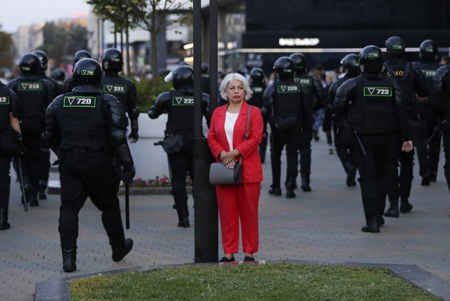 A woman stands in a street as police gather to block protesters during a mass protest following presidential elections in Minsk, Belarus, Monday, August 10, 2020. (Photo by Sergei Grits/AP Photo)
