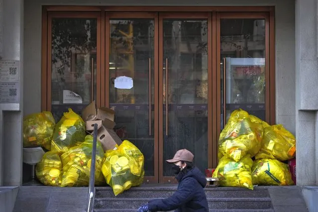 A woman rides past protective suits and household trash inside yellow trash bags marked as medical waste gathered outside at a hotel entrance door in Beijing, Sunday, December 11, 2022. (Photo by Andy Wong/AP Photo)