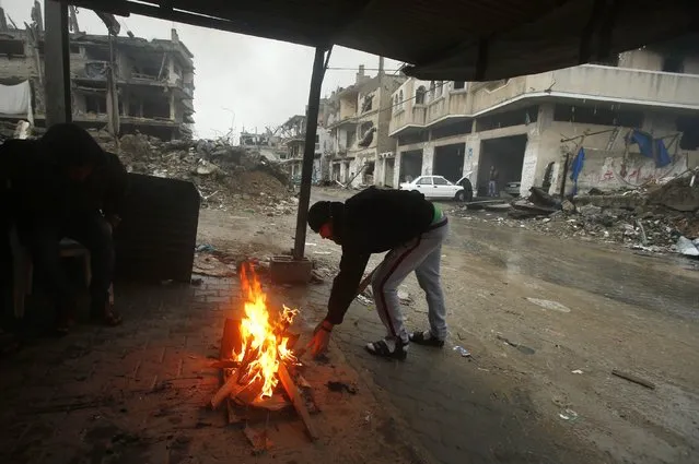A Palestinian man lights a fire to warm himself in a makeshift shelter near houses that witnesses said were destroyed or damaged by Israeli shelling during the most recent conflict between Israel and Hamas, on a rainy day in the east of Gaza City November 16, 2014. (Photo by Suhaib Salem/Reuters)