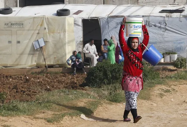 A Syrian refugee girl carries a bucket of water as she walks past tents at a refugee camp in Zahle in the Bekaa valley November 18, 2014. (Photo by Mohamed Azakir/Reuters)
