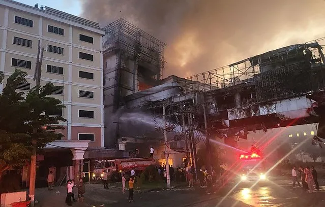 Firefighters spray water onto the site of a fire at the Grand Diamond City hotel-casino in Poipet on December 29, 2022. As many as 10 people have died in a fire at a Cambodian hotel-casino on the border of Thailand, with photos showing groups desperately huddled on ledges as fierce flames surround them. (Photo by AFP Photo/Stringer)