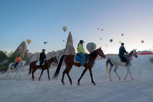 Hot air balloons rise as people ride horse at Cappadocia, which held a special place for horses throughout history, in Nevsehir, Turkiye on June 29, 2025. Visitors to the region can join guided horseback tours held in the wide valleys, especially during morning and evening hours. Located within the borders of Nevehir, Cappadocia stands out not only for its natural formations but also for its rich cultural heritage. (Photo by Ayten Altintas/Anadolu via Getty Images)