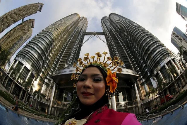 A woman in traditional dress poses for a picture in front of the Petronas towers in downtown Kuala Lumpur, Malaysia, November 22, 2015. Picture taken with a fisheye lens. (Photo by Jorge Silva/Reuters)