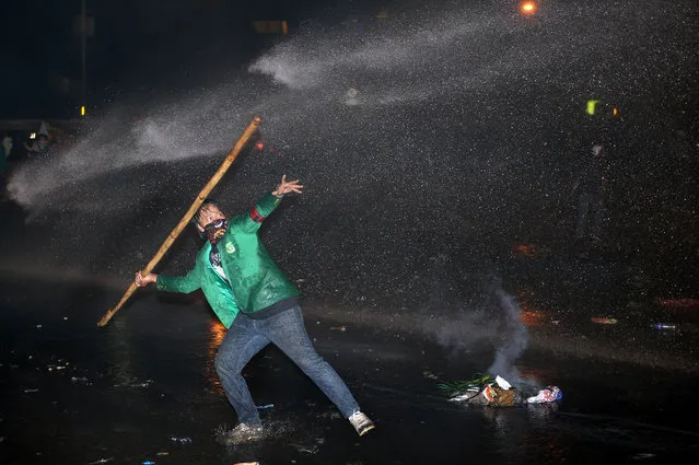 An Indonesian student hurls a bamboo stick as police spray a water cannon during a protest against the fuel price hike outside parliament in Jakarta on June 17, 2013.  Police fired tear gas and rubber bullets at stone-throwing protesters in Indonesia on June 17, as thousands demonstrated nationwide against the government's plan to increase fuel prices. (Photo by Adek Berry/AFP Photo)