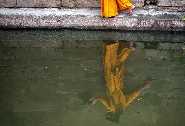 A Hindu devotee makes her way back through a narrow ledge on the banks of the Bagmati river after offering prayers in front of an idol of Astamatrika, representing eight divine mother goddesses, at the Pashupatinath temple premises in Kathmandu, Nepal, Thursday, April 20, 2023. Nepalese Hindus on Thursday were marking Matatirtha Aunshi festival during which they pay tribute to their deceased mothers. (Photo by Niranjan Shrestha/AP Photo)