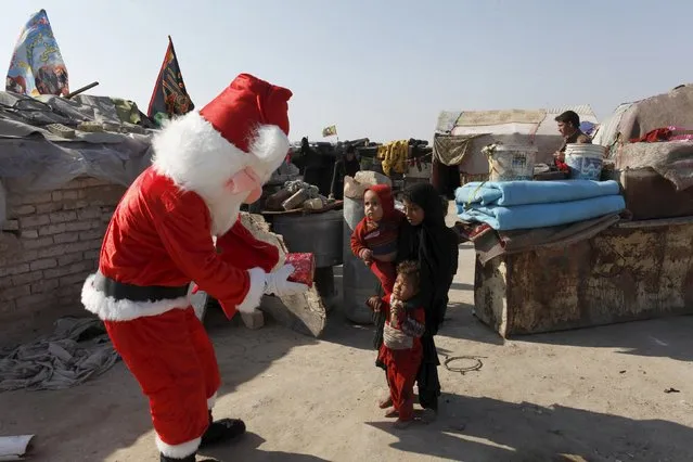 A man wearing a Santa Claus costume distributes presents to children at a poor community in Najaf, south of Baghdad, December 19, 2015. (Photo by Alaa Al-Marjani/Reuters)