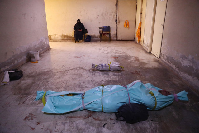 A woman sits facing two covered bodies at a make-shift morgue following government shelling on the rebel-held town of Douma, on the eastern outskirts of Damascus, on November 10, 2016. At least 11 people including four children were killed in air strikes on rebel-held areas near the Syrian capital, the Syrian Observatory for Human Rights said. (Photo by Abd Doumany/AFP Photo)