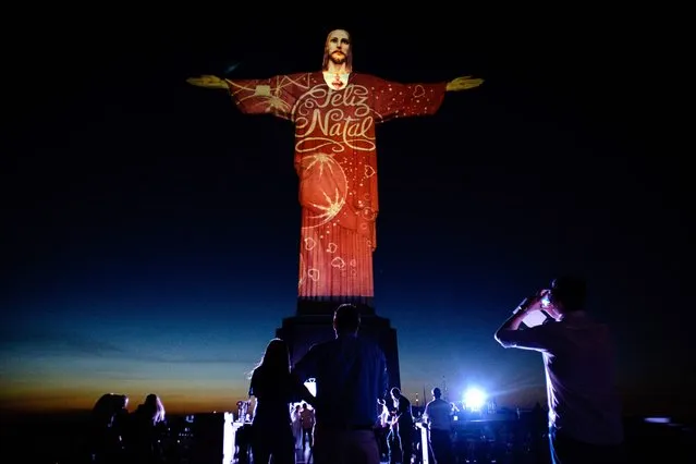 People take pictures of the statue of Christ the Redeemer illuminated by Brazil-based French lighting designer Gaspare Di Caro reading “Merry Christmas” at the Corcovado hill in Rio de Janeiro, Brazil, on December 23, 2015. (Photo by Yasuyoshi Chiba/AFP Photo)