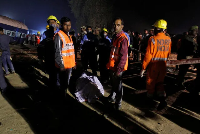 Rescue workers stand beside the remains of a passenger at the site of a train derailment in Pukhrayan, south of Kanpur city, India November 20, 2016. (Photo by Jitendra Prakash/Reuters)