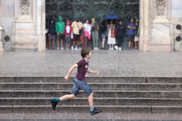 A boy runs under heavy rain as tourists take shelter under the Duomo Cathedral during a storm, in Milan, Italy on July 6, 2023. (Photo by Claudia Greco/Reuters)