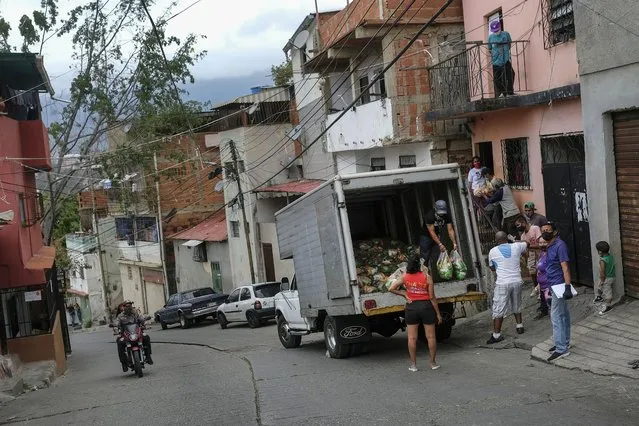 Residents help to unload bags of basic food staples, such as pasta, sugar, flour and kitchen oil, provided by a government food assistance program, as a couple on a motorcycle drive past in front of they in the Santa Rosalia neighborhood of Caracas, Venezuela, Saturday, April 10, 2021. (Photo by Matias Delacroix/AP Photo)