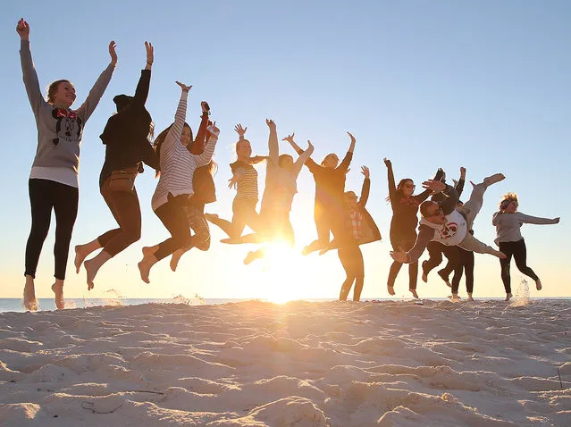 In this photo taken Tuesday, January 19, 2016, visitors from Australia jump as they take a photo taken at sunset along the beach in Panama City Beach, Fla. The group made a stop in Panama City Beach as part of a bus tour from Los Angeles to New York City. (Photo by Andrew Wardlow/News Herald via AP Photo)