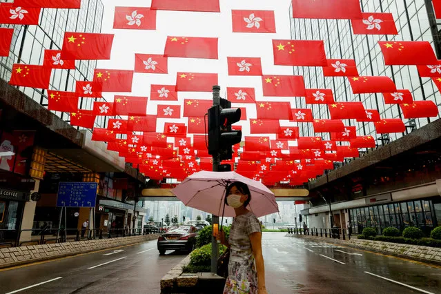 A woman walks under China and Hong Kong's flags hanging outside a shopping mall ahead of the 100th founding anniversary of the Communist Party of China, in Hong Kong, China on June 28, 2021. (Photo by Tyrone Siu/Reuters)