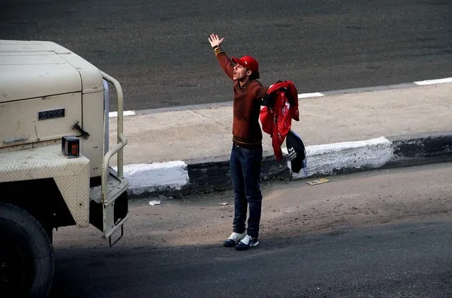 A supporter of Egyptian club Al Ahly gestures in front of a military vehicle outside a stadium ahead of the African Champions League final in Cairo, on November 10, 2013. Hundreds of supporters of Al Ahly clashed with police ahead of the match. Police used tear gas to disperse the crowd as they threw rocks and tried to push their way into the stadium, many with no tickets. (Photo by Mostafa Darwish/Associated Press)