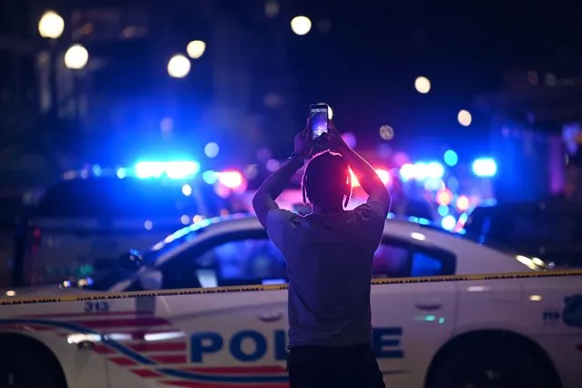 A man uses his phone in front of police cars blocking a street after a shooting at a restaurant in Washington, DC, on July 22, 2021. (Photo by Brendan Smialowski/AFP Photo)