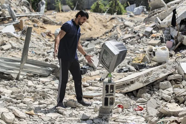 Palestinian performance artist Mohammed al-Shenbari stacks up a television atop a bottle standing on a piece of rubble as he demonstrates his skills in balancing objects atop each other, in the ruins of houses destroyed by Israeli air strikes during the May 2021 conflict between Israel and Hamas, in Beit Lahia in the northern Gaza Strip on July 6, 2021. The self-taught 26-year-old artist says he can balance almost any object, through his training in fitness and body-building. (Photo by Mohammed Abed/AFP Photo)
