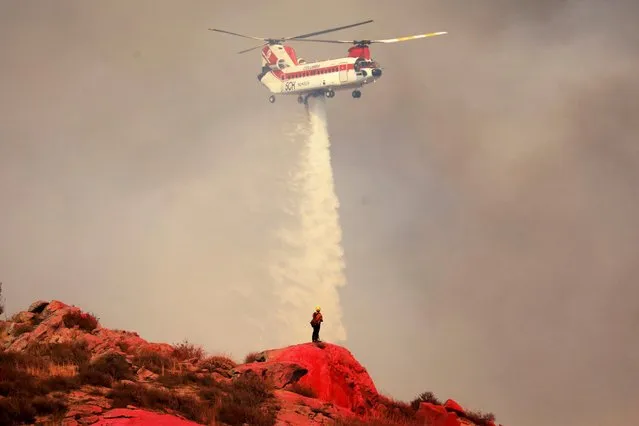 Water is dropped near a fireman standing on fire retardant painted hillside as the Fairview Fire burns near Hemet, California, U.S., September 6, 2022. (Photo by David Swanson/Reuters)