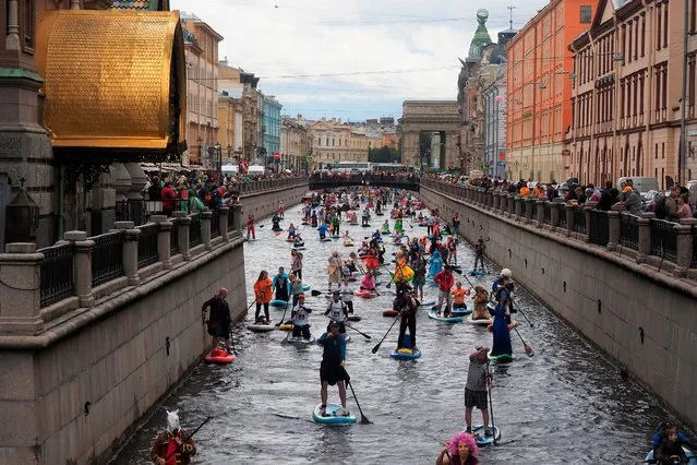 People steer their paddle-boards along a channel during a SUP (Stand Up Paddle)-Surfing festival in St.Petersburg, Russia, Saturday, July 31, 2021. Thousands of costumed participants of a standup paddle-boarding festival will get together to go nine Kilometres (5,6 miles) along central rivers and canals of St Petersburg, passing by major tourist sites and competing in fun categories such as The Best SUP Board Design or The Most Original Costume made of Recycled Materials. (Photo by AP Photo/Stringer)