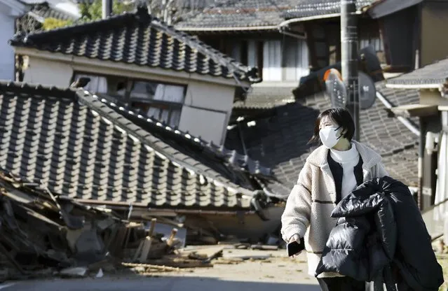 A woman walks in front of collapsed houses following earthquake in Noto-cho, Ishikawa prefecture, Japan Tuesday, January 2, 2024. A series of powerful earthquakes hit western Japan, damaging buildings, vehicles and boats, with officials warning people in some areas on Tuesday to stay away from their homes because of a risk of more strong quakes. (Photo by Kyodo News via AP Photo)