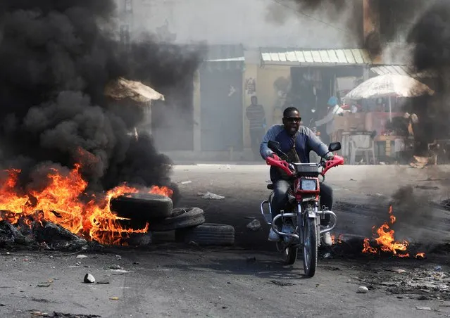 A motorcyclist reacts while driving through a burning barricade, one of many across several neighbourhoods that forced residents to take shelter, in Port-au-Prince, Haiti on January 18, 2024. (Photo by Ralph Tedy Erol/Reuters)