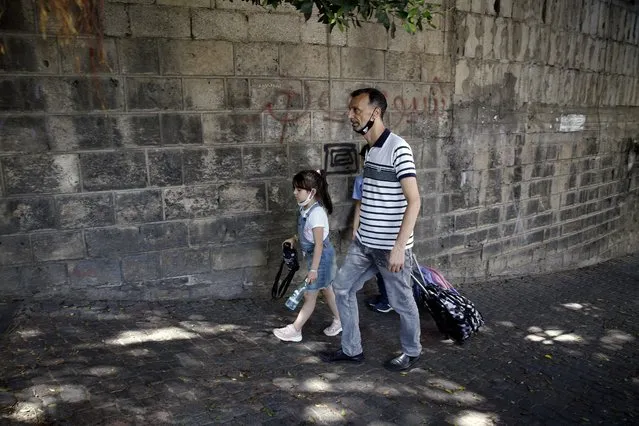 A man walks with his children at the end of their school day in Beirut, Lebanon, Wednesday, September 29, 2021. Lebanese students are returning to schools, many for the first time since late 2019, but the country's crippling economic crisis is threatening to derail the first in-class academic year after the pandemic. Public school teachers are on strike, demanding their pay be adjusted to make up for the collapse of the national currency, and a severe fuel shortage threatens to keep classrooms dark. (Photo by Bilal Hussein/AP Photo)