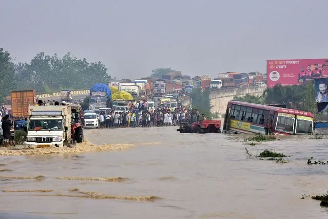 Commuters stand on a flyover on a flooded national highway after river Kosi overflowed following heavy rains near Rampur in India's Uttar Pradesh state on October 20, 2021, as the death toll from days of flooding and landslides in India and Nepal crossed 100. (Photo by AFP Photo/Stringer)