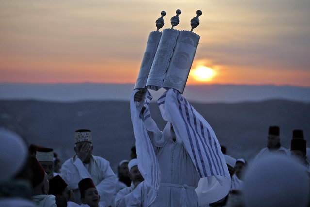 A Samaritan priest raises the Torah scroll as worshippers gather to pray a passover ceremony on top of Mount Gerizim near the northern West Bank city of Nablus early on April 25, 2019. The Samaritans are a community of a few hundred people living in Israel and in the Nablus area who trace their lineage to the ancient Israelites led by the biblical prophet Moses out of Egypt. (Photo by Jaafar Ashtiyeh/AFP Photo)