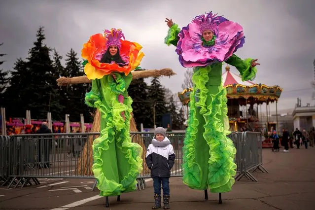 A child poses with entertainers on stilts during a show of traditions for Masnytsia, a holiday that originates in pagan times, celebrating the end of winter, in Kyiv, Ukraine, Saturday, March 16, 2024. (Photo by Vadim Ghirda/AP Photo)