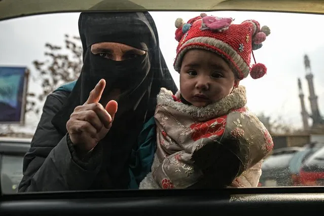 A woman carries a child as she begs from commuters in a car in Kabul on December 26, 2021. (Photo by Mohd Rasfan/AFP Photo)