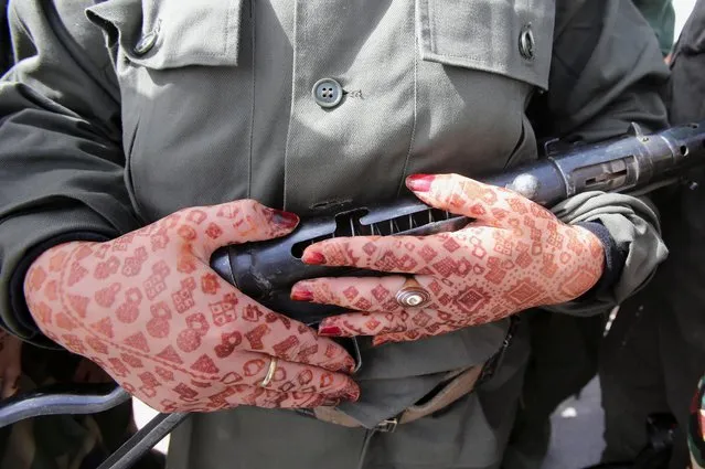 A Sahrawi woman soldier, with henna dyed patterns on her hands, carries a weapon during a parade at the Awserd refugee camp in Tindouf, Algeria on February 27, 2021. (Photo by Ramzi Boudina/Reuters)