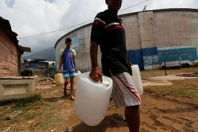 Men carrying plastic containers used for water, walk in front of a non-operative water tank, in the neighbourhood called “The Tank” at the slum of Petare in Caracas, Venezuela, April 3, 2016. (Photo by Carlos Garcia Rawlins/Reuters)