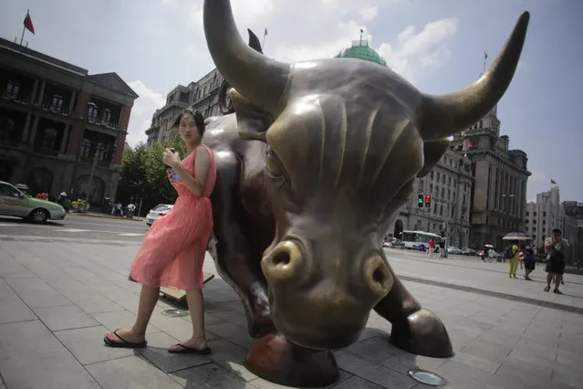 A visitor stands near “Charging Bull” statue in Shanghai, China, Monday, July 22, 2013. (Photo by Eugene Hoshiko/AP Photo)