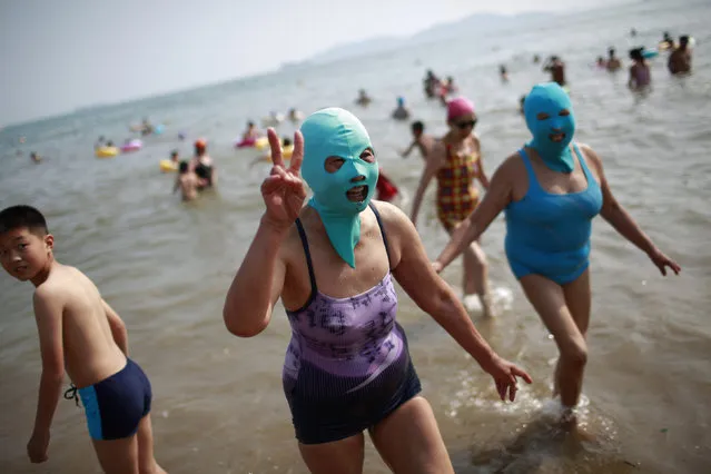 A woman, wearing a nylon mask, flashes a sign as she walks towards the shore during her visit to a beach in Qingdao, Shandong province July 6, 2012. (Photo by Aly Song/Reuters)