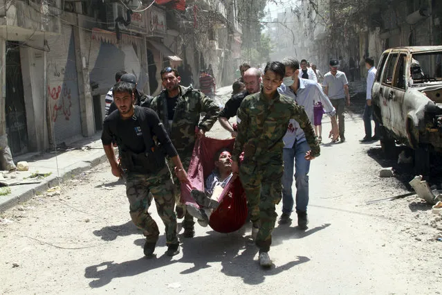 Rescuers carry a man wounded by a mine that went off in the Bustan al-Diwan neighborhood of Homs, Syria, Saturday, May 10, 2014. Thousands of Syrians streamed into war-battered parts of the central city of Homs for the first time in nearly two years Saturday, many making plans to move back just days after rebels surrendered their strongholds to pro-government forces. (Photo by AP Photo)