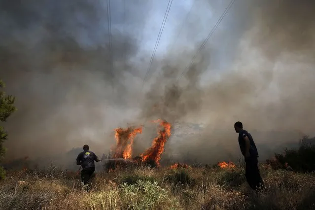 Municipality workers try to extinguish flames burning on the mountain of Ymittos in Athens, Friday, July 17, 2015. (Photo by Petros Giannakouris/InTime News via AP Photo)