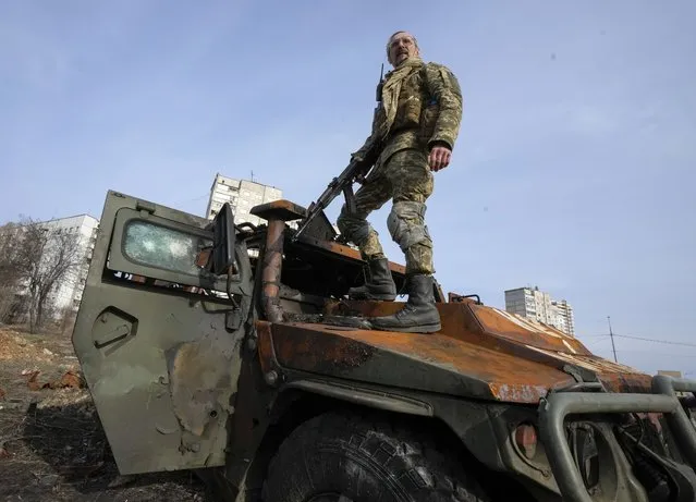 A Ukrainian soldier stands a top a destroyed Russian APC after recent battle in Kharkiv, Ukraine, Saturday, March 26, 2022. With Russia continuing to strike and encircle urban populations, from Chernihiv and Kharkiv in the north to Mariupol in the south, Ukrainian authorities said Saturday that they cannot trust statements from the Russian military Friday suggesting that the Kremlin planned to concentrate its remaining strength on wresting the entirety of Ukraine's eastern Donbas region from Ukrainian control. (Photo by Efrem Lukatsky/AP Photo)