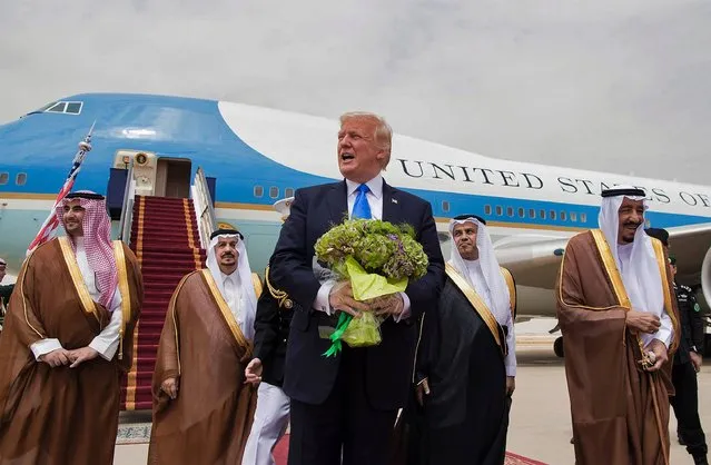 US President Donald Trump (C) holds a bouquet of flowers upon being welcomed by Saudi King Salman bin Abdulaziz al-Saud (R) during the former's arrival at King Khalid International Airport in Riyadh on May 20, 2017. (Photo by Bandar Al-Jaloud/AFP Photo/Saudi Royal Palace)