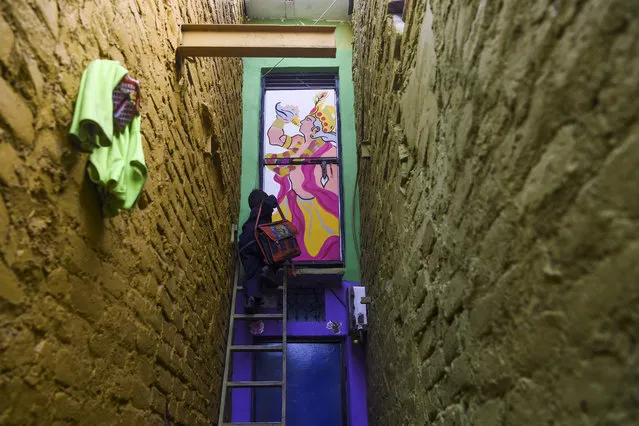 A boy climbs up a ladder to enter a home adorned with a mural painted by artists from “Delhi Street Art” group at the Raghubir Nagar slum in New Delhi on December 2, 2019. (Photo by Sajjad Hussain/AFP Photo)