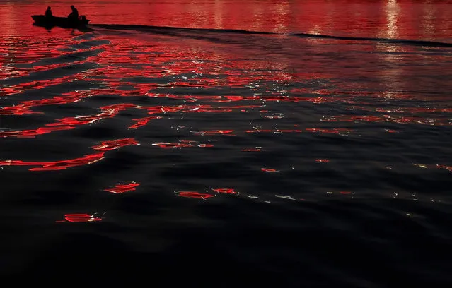 A boat floats through light reflected from the illuminated Ada Bridge over the Sava river in Belgrade, Serbia, late Monday, July 20, 2015. (Photo by Darko Vojinovic/AP Photo)