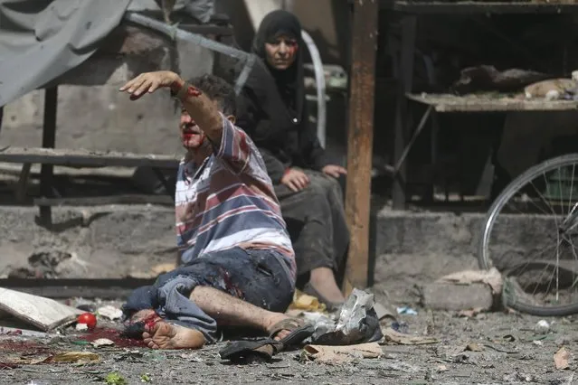 An injured man gestures as he sits near a wounded woman after what activists said were airstrikes by forces loyal to Syria's President Bashar al-Assad on a busy marketplace in the Douma neighborhood of Damascus, Syria August 12, 2015. (Photo by Bassam Khabieh/Reuters)